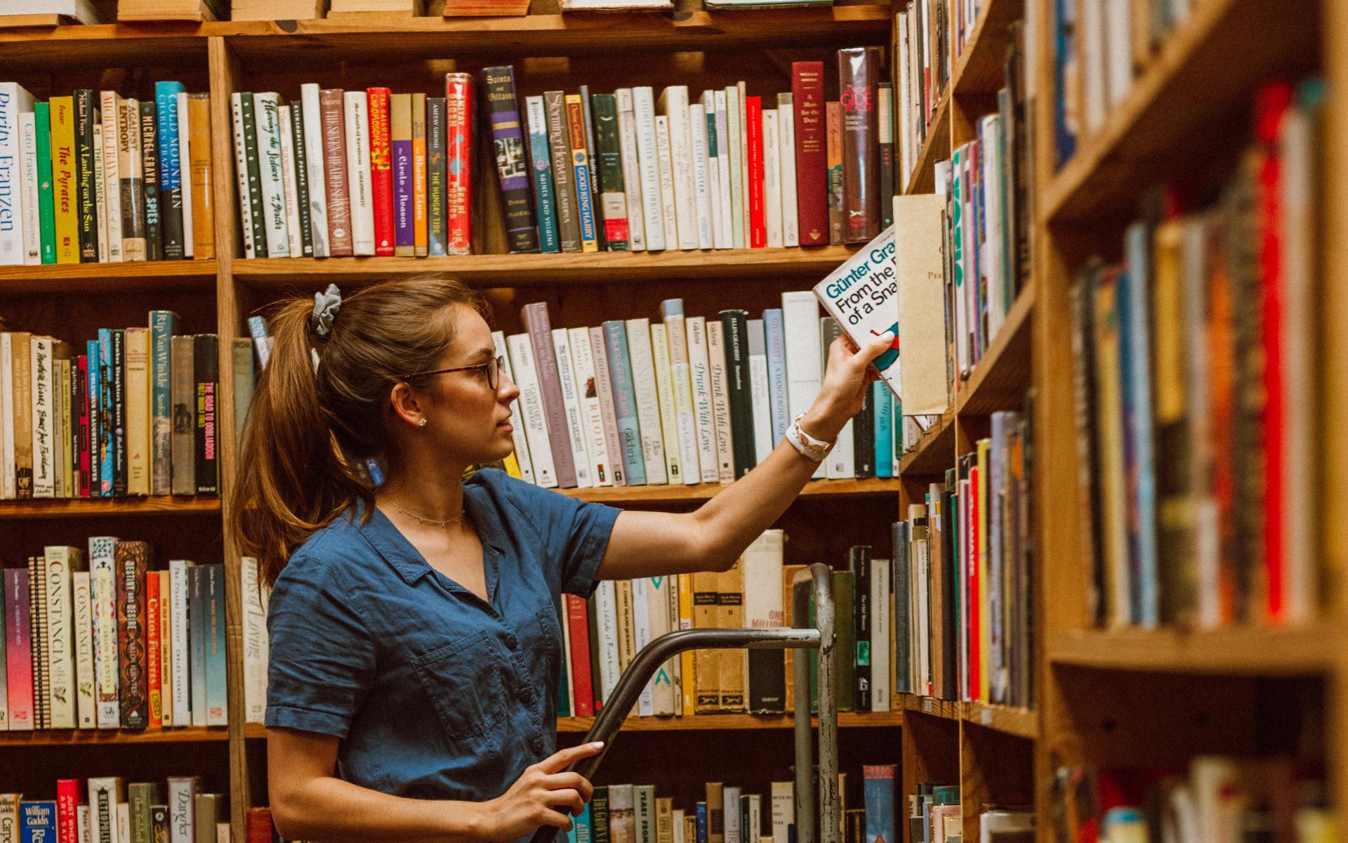 Junge Frau auf einer Leiter vor dem Bücherregal